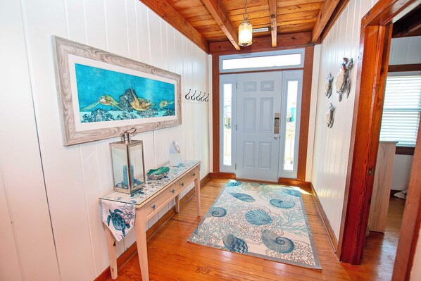 A hallway with wooden flooring, a framed painting of sea turtles, a glass display case, a wooden bench, and a patterned rug. - OCEANFRONT, Ocean views, Dogs Welcome! KH10, Beach House (Kitty Hawk)