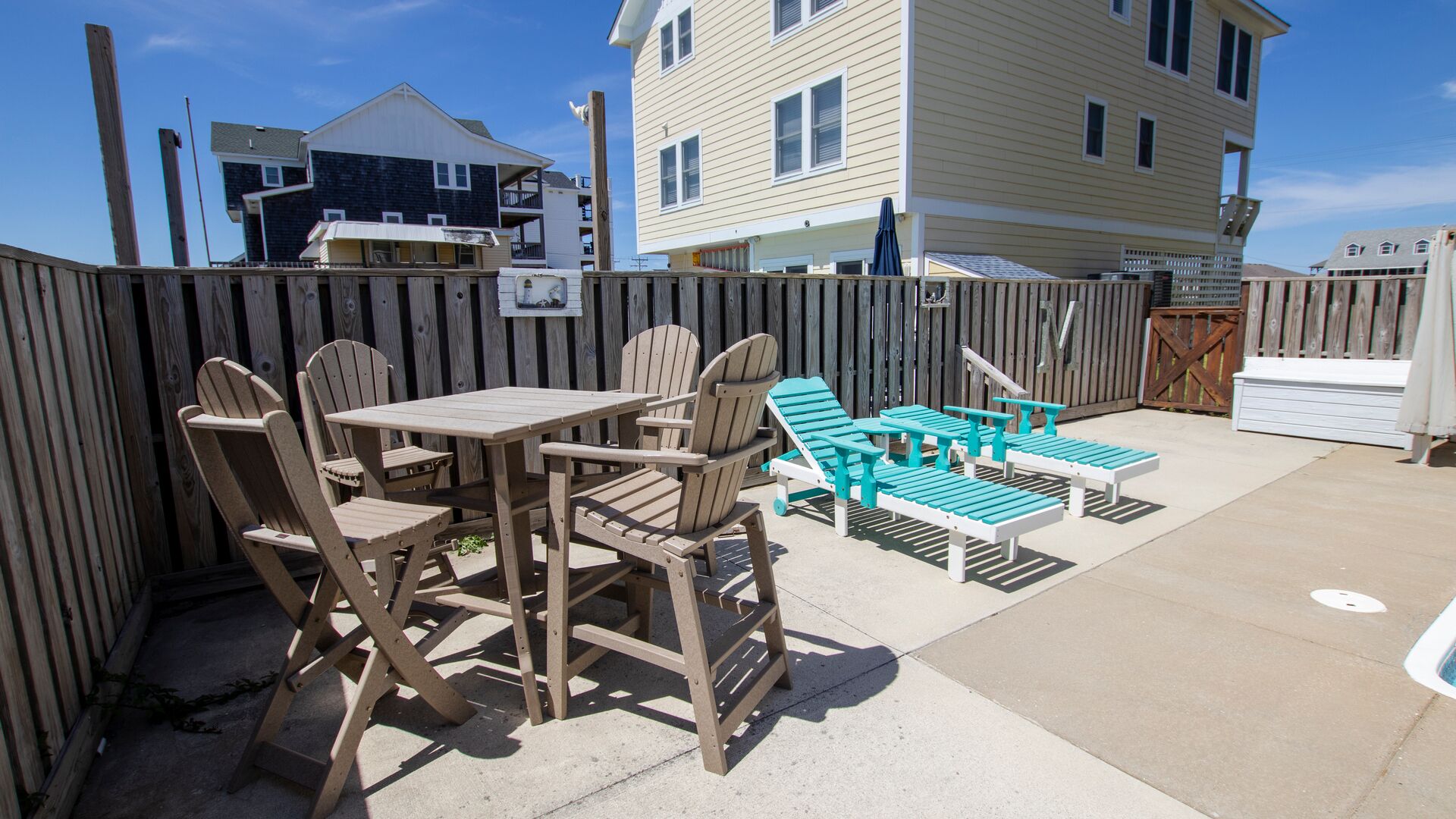 A patio with wooden chairs and tables, a small table with a blue tablecloth, and a wooden fence.