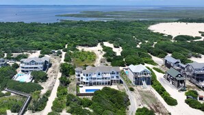 Une propriété située sur la côte, comprenant plusieurs bâtiments, une plage et une vaste étendue d’eau.