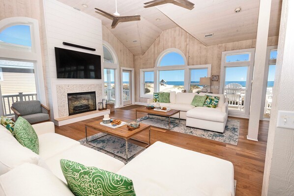 A spacious living room with a fireplace, large windows, and a view of the beach.