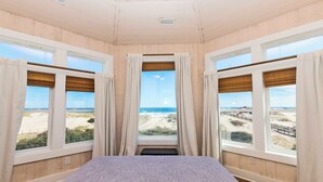 Une chambre avec un lit, de grandes fenêtres et vue sur la plage.