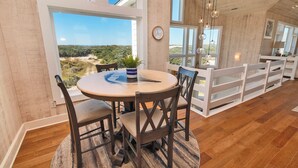Un espace repas comprenant une table ronde, des chaises et une vue sur le paysage grâce à de grandes fenêtres.