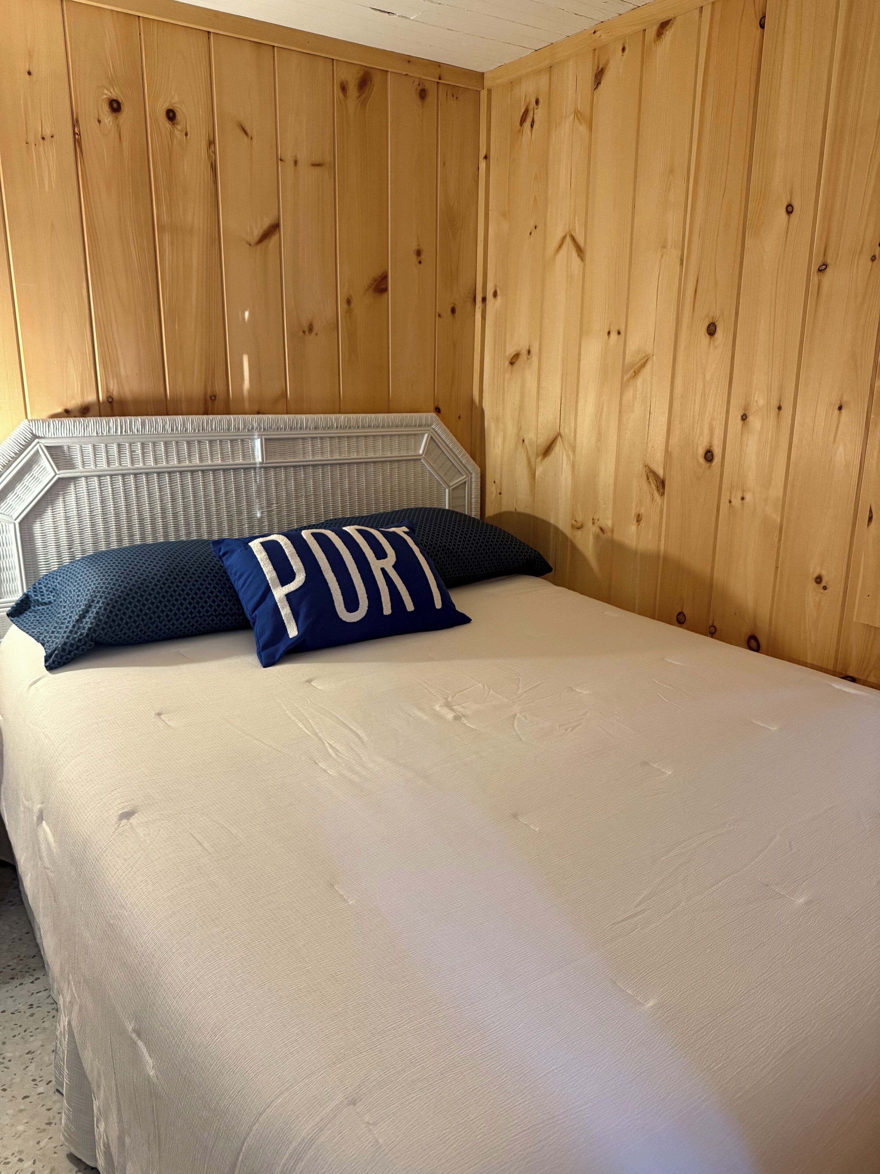 A bed with a white mattress, a metal headboard, and a blue pillow with the word "PORT" on it.