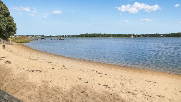 A sandy beach with calm water, a pier, and a distant shoreline with buildings. -  Steps to private Beach, Golf Course, AC, tandem Kayak for Guests (South Yarmouth)