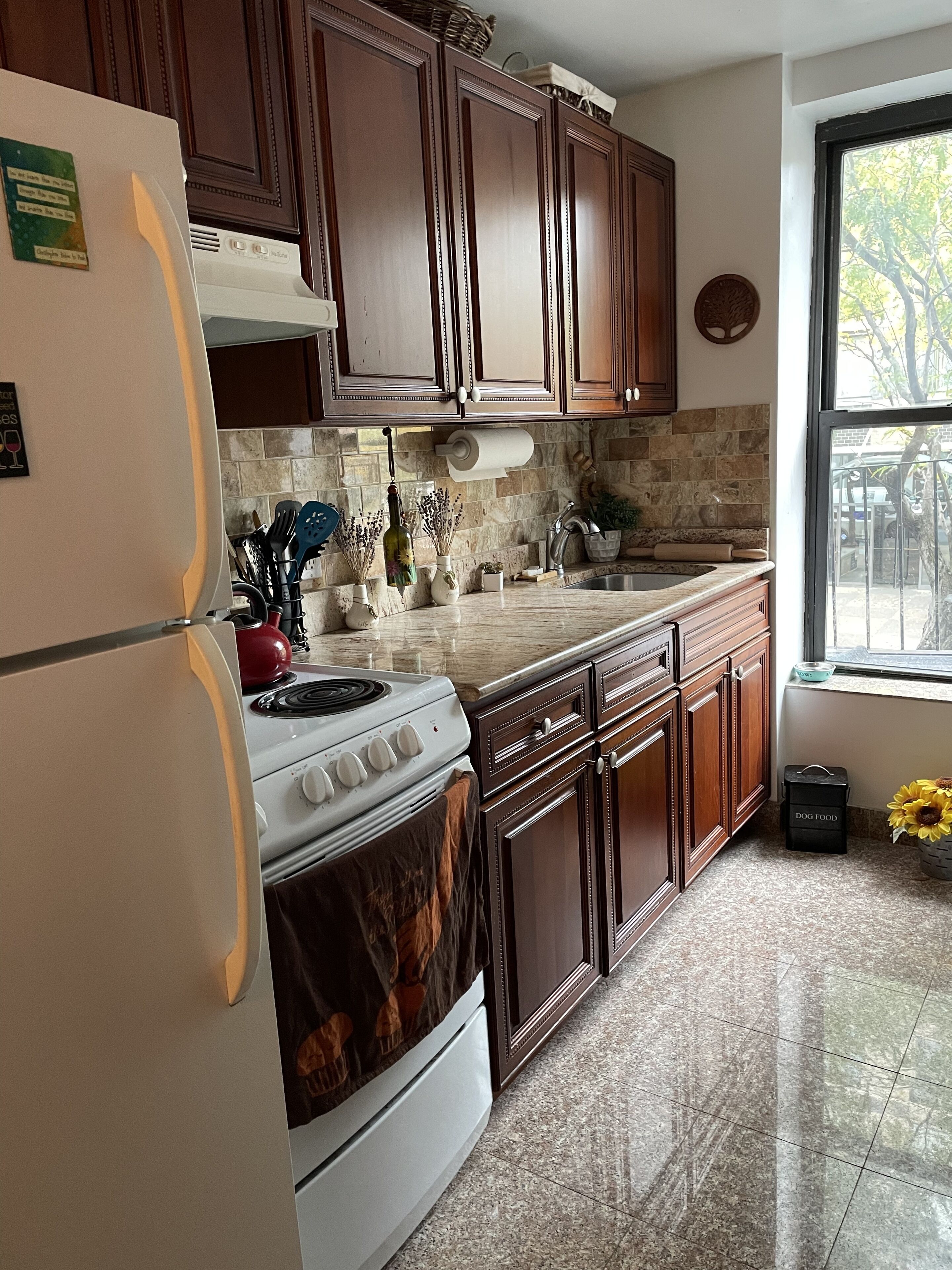 A kitchen with wooden cabinets, a white refrigerator, a stove, and a window with a view of trees.