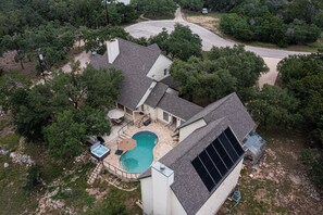 Vue aérienne d’une propriété résidentielle dotée d’une piscine, de panneaux solaires et d’une allée menant à une entrée sécurisée par un portail.