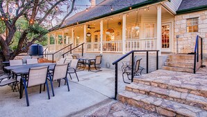 Un patio exterior con escalones de piedra que llevan a una zona de estar cubierta, amueblada con mesas y sillas.