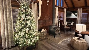 L’intérieur d’un chalet rustique, avec un sapin de Noël décoré, des murs en bois, un poêle en pierre et un coin repas.
