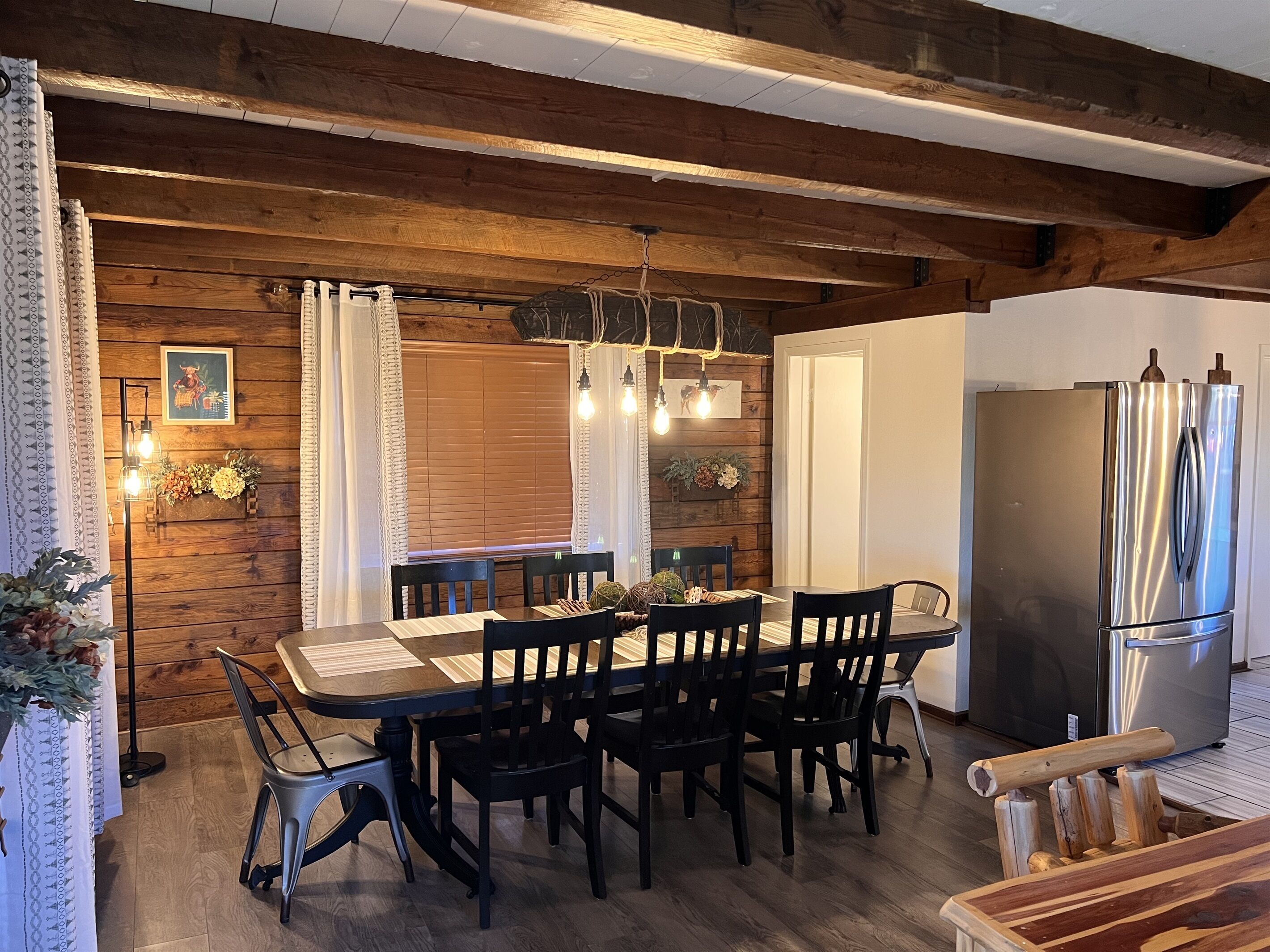 Un comedor con una mesa y sillas de madera, un refrigerador moderno y una lámpara colgante.