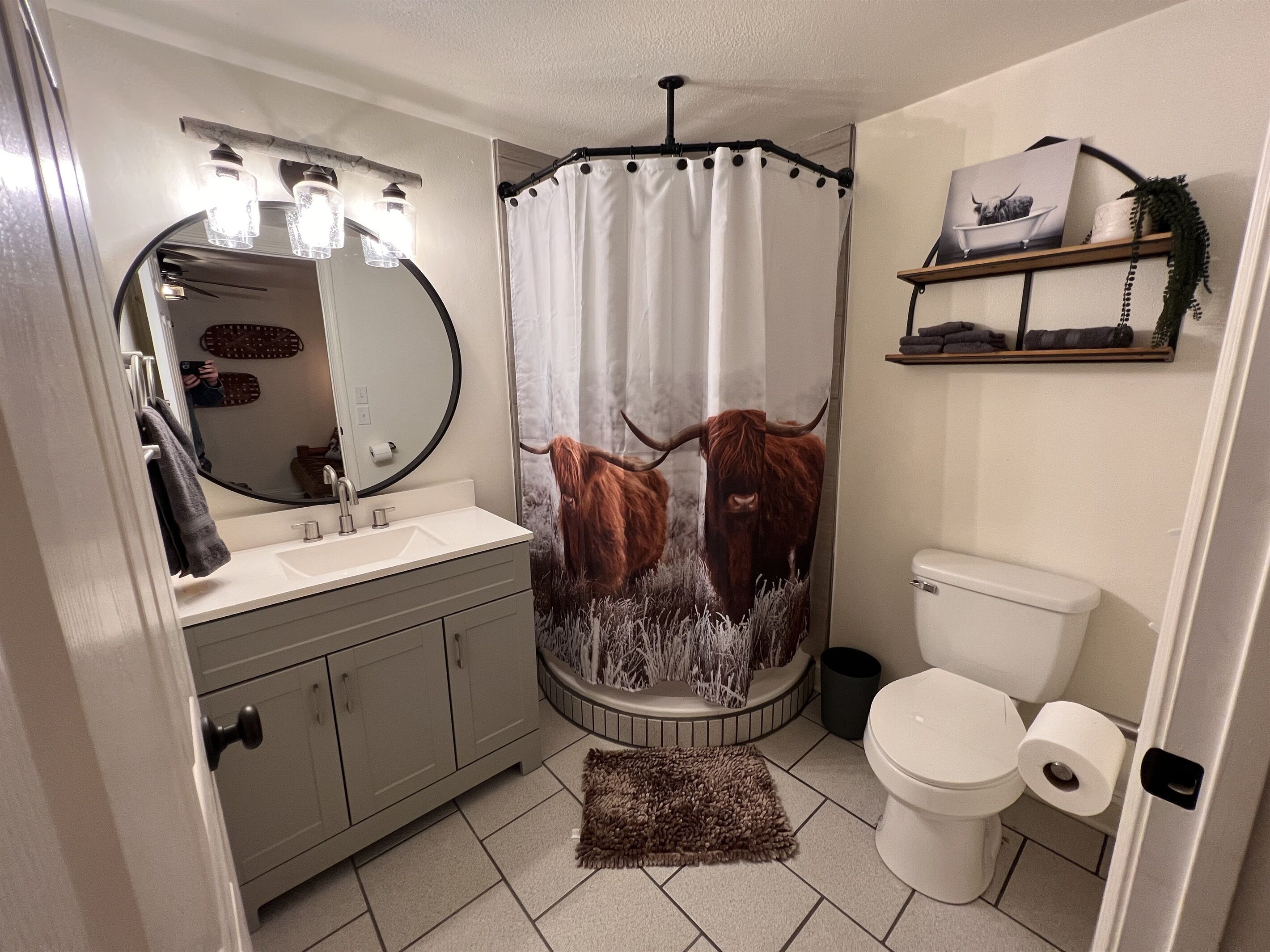 Un baño con lavamanos, espejo, inodoro y cortina de ducha con diseño de vaca de las tierras altas.