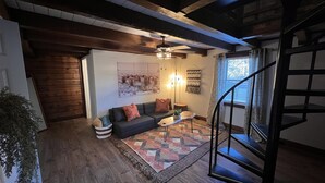 Un salon chaleureux avec un canapé aux couleurs sombres, un tapis à motifs et un escalier sur le côté droit.