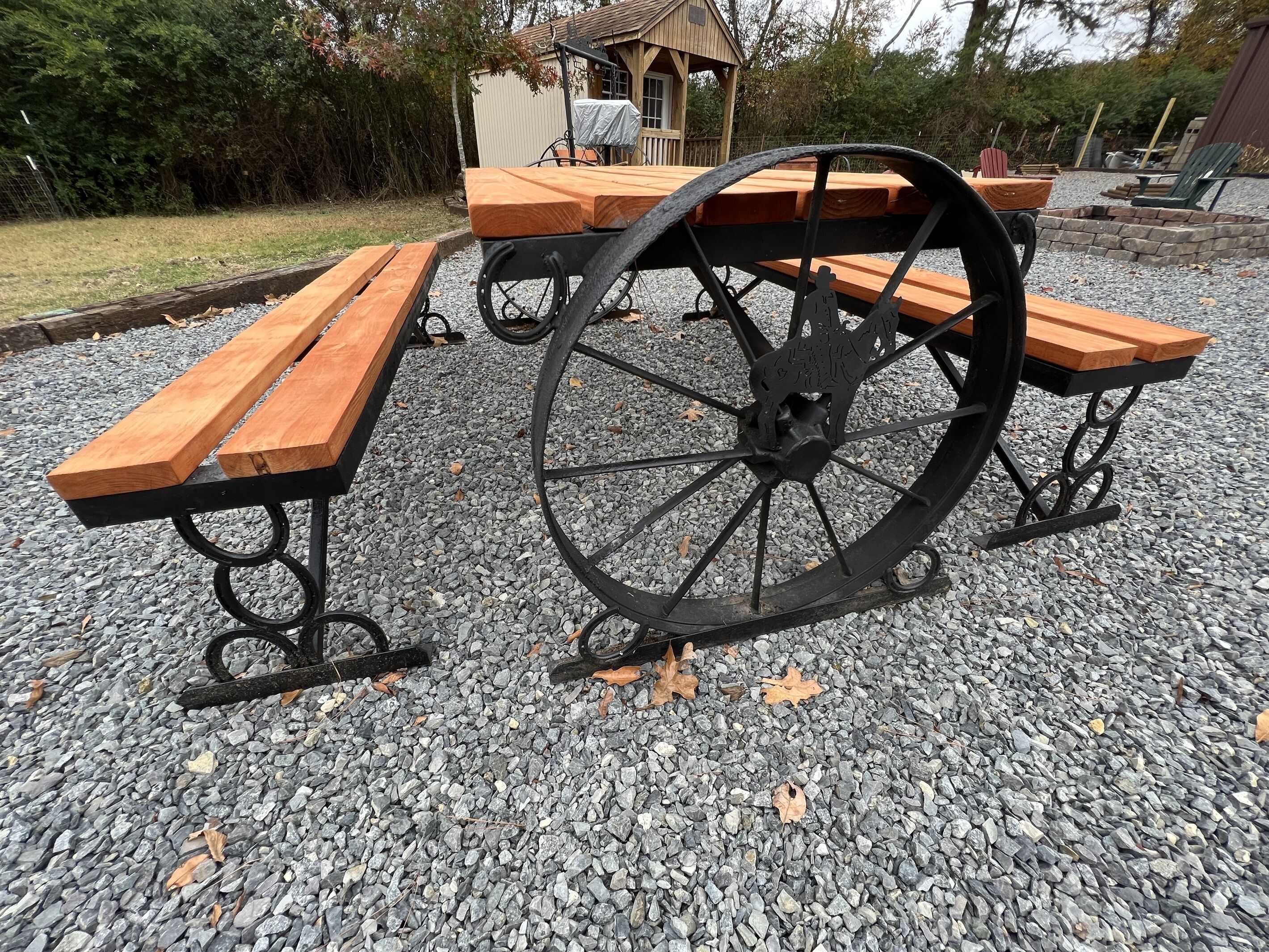 Une table de pique-nique dotée d’une grande roue, entourée de gravier et de bancs en bois.