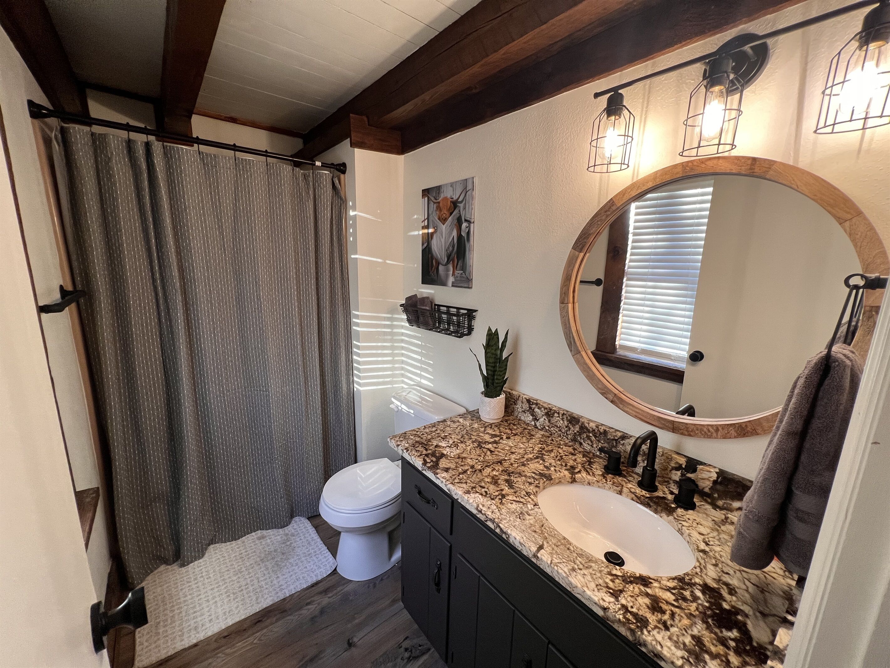 A bathroom with a shower curtain, toilet, sink, vanity, mirror, and towel rack.