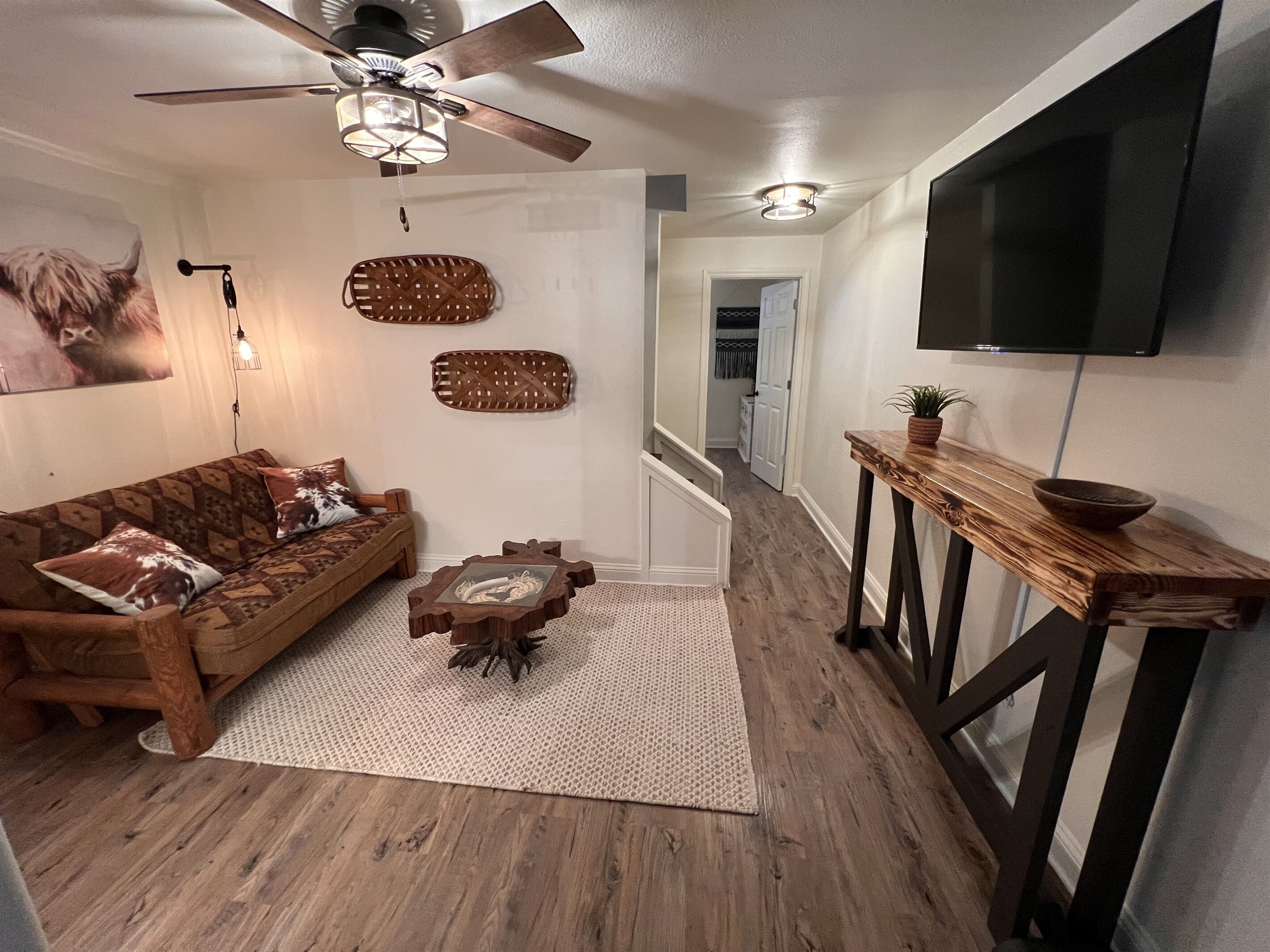 A cozy living room with a wooden sofa, a coffee table, and a TV mounted on the wall.