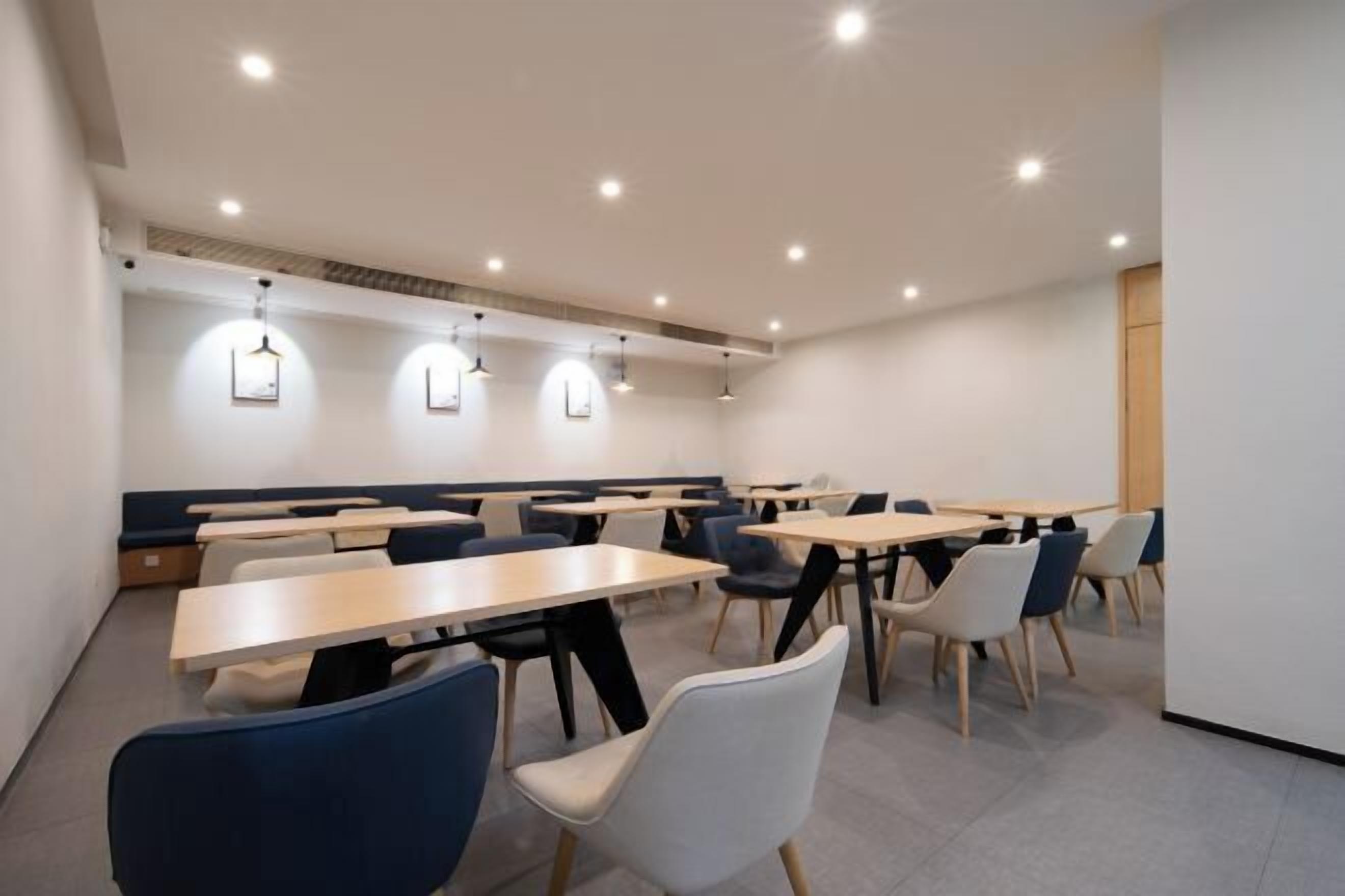 Un comedor moderno con varias mesas y sillas, luces empotradas en el techo y una pared decorativa de madera.