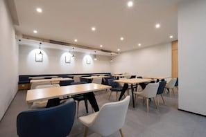 A modern dining area with multiple tables and chairs, recessed ceiling lights, and a wooden accent wall.