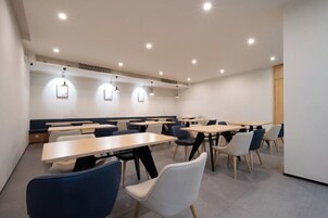 A modern dining area with multiple tables and chairs, recessed ceiling lights, and a wooden accent wall.