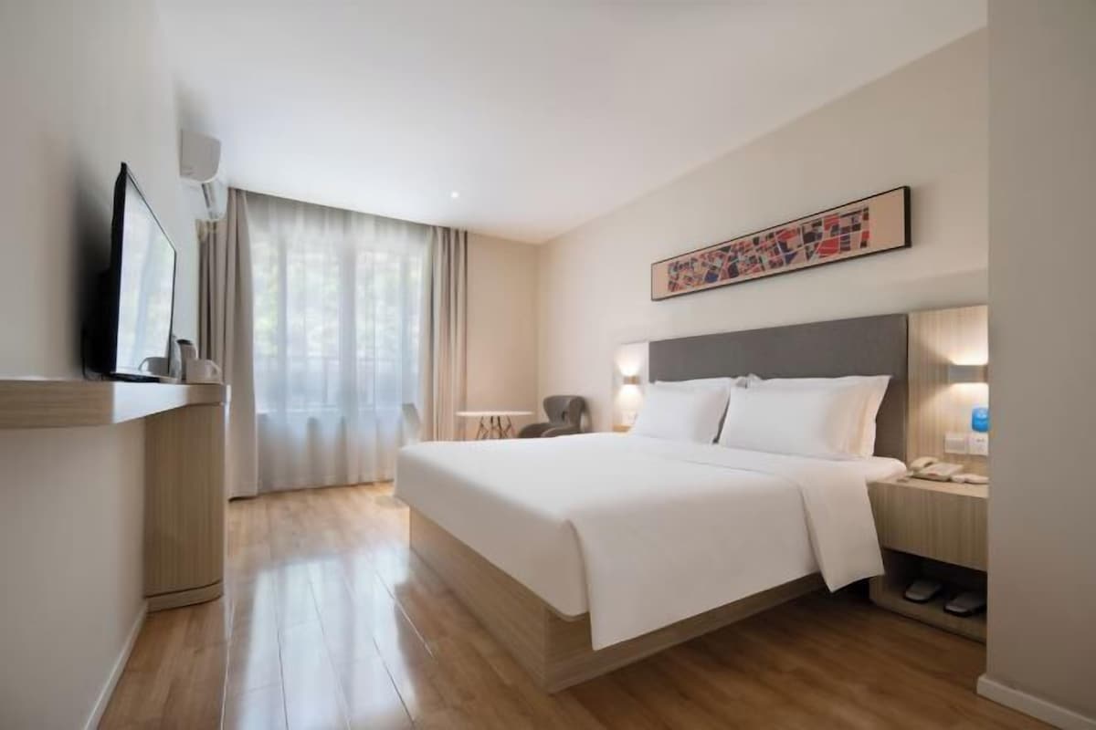 Ein Hotelzimmer mit einem großen Bett, einem Schreibtisch, einem Sessel, einem Fernseher und einem Fenster mit Vorhängen.