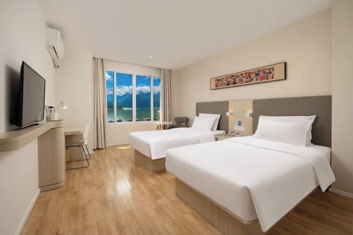 A hotel room with two beds, a TV, a desk, and a window with a view of mountains.