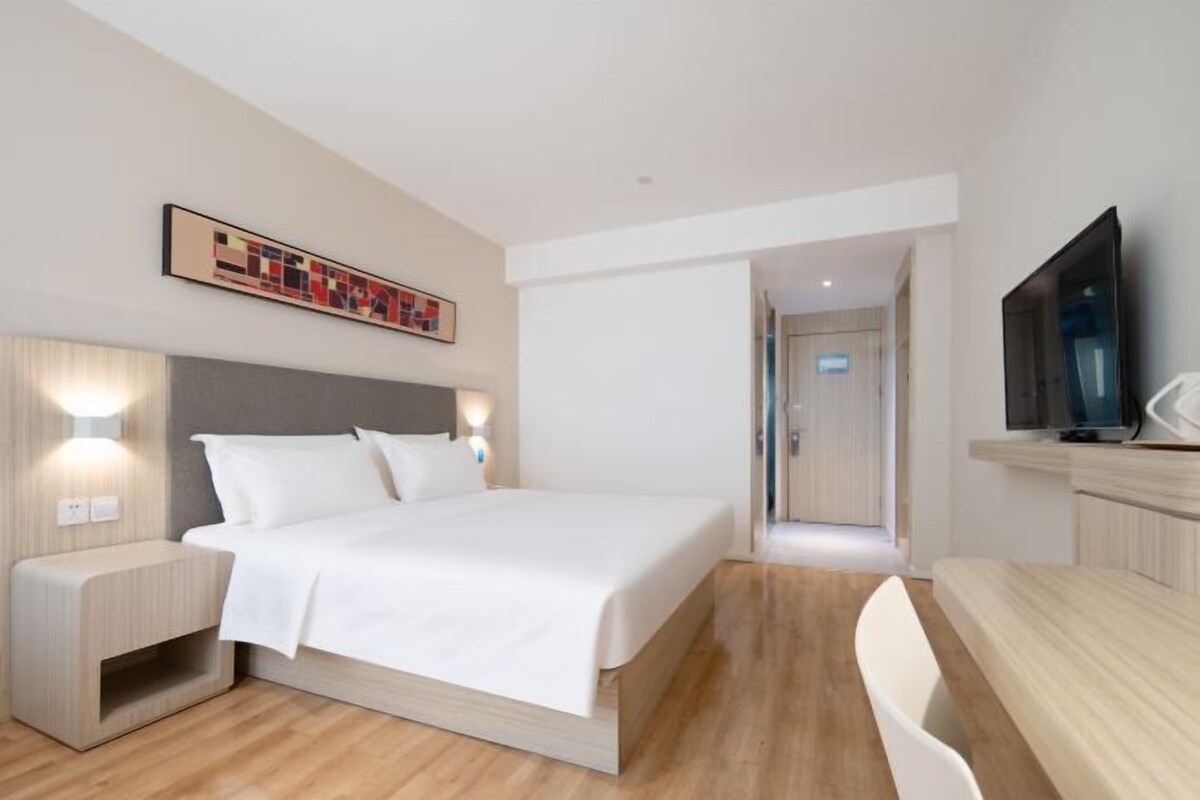 Una moderna camera d'albergo con un letto grande, lampade ai comodini, una TV a schermo piatto e un pavimento in legno.