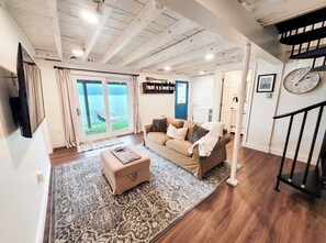 Relax in this spacious living area with a high ceiling, featuring a sofa, ottoman, and flat-screen TV.