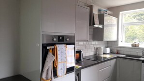 A modern kitchen with white cabinets, a built-in oven, a microwave, and a window providing natural light. - Beautiful modern 3-Bed House in Birmingham (Birmingham)