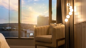 A modern hotel room with a large window, a comfortable armchair, and a floor lamp with multiple lights. - Black Marble - Menlyn Residence (Pretoria)