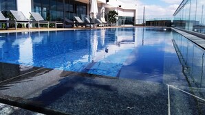 A modern indoor swimming pool with clear blue water, sun loungers, and umbrellas. - Black Marble - Menlyn Residence (Pretoria)