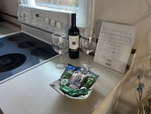 A kitchen counter with a bottle of wine, two glasses, a note, and a tray of snacks.