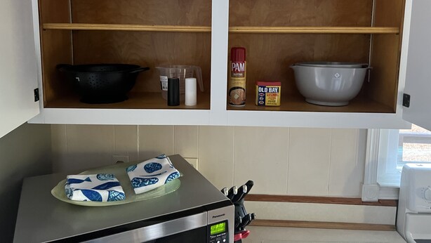 Une cuisine avec des étagères en bois, une poêle noire, un saladier blanc, un verre à mesurer, un récipient de beurre PAM et un récipient d’épices Old Bay.