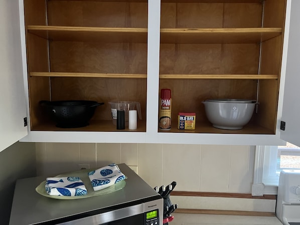A kitchen with wooden shelves, a black frying pan, a white bowl, a measuring cup, a container of PAM butter, and a container of Old Bay seasoning.