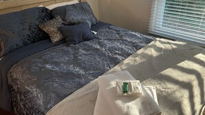 Un lit bien fait, avec une couvre-lit à motifs, une tête de lit et une fenêtre équipée de stores.