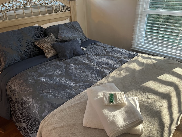 A neatly made bed with a patterned bedspread, a headboard, and a window with blinds.
