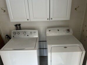 A laundry room with two white washing machines and a dryer, a white cabinet above, and a wall-mounted towel rack. - Cozy Cottage with access to and partially obstructed views of the bay. (Port Republic)