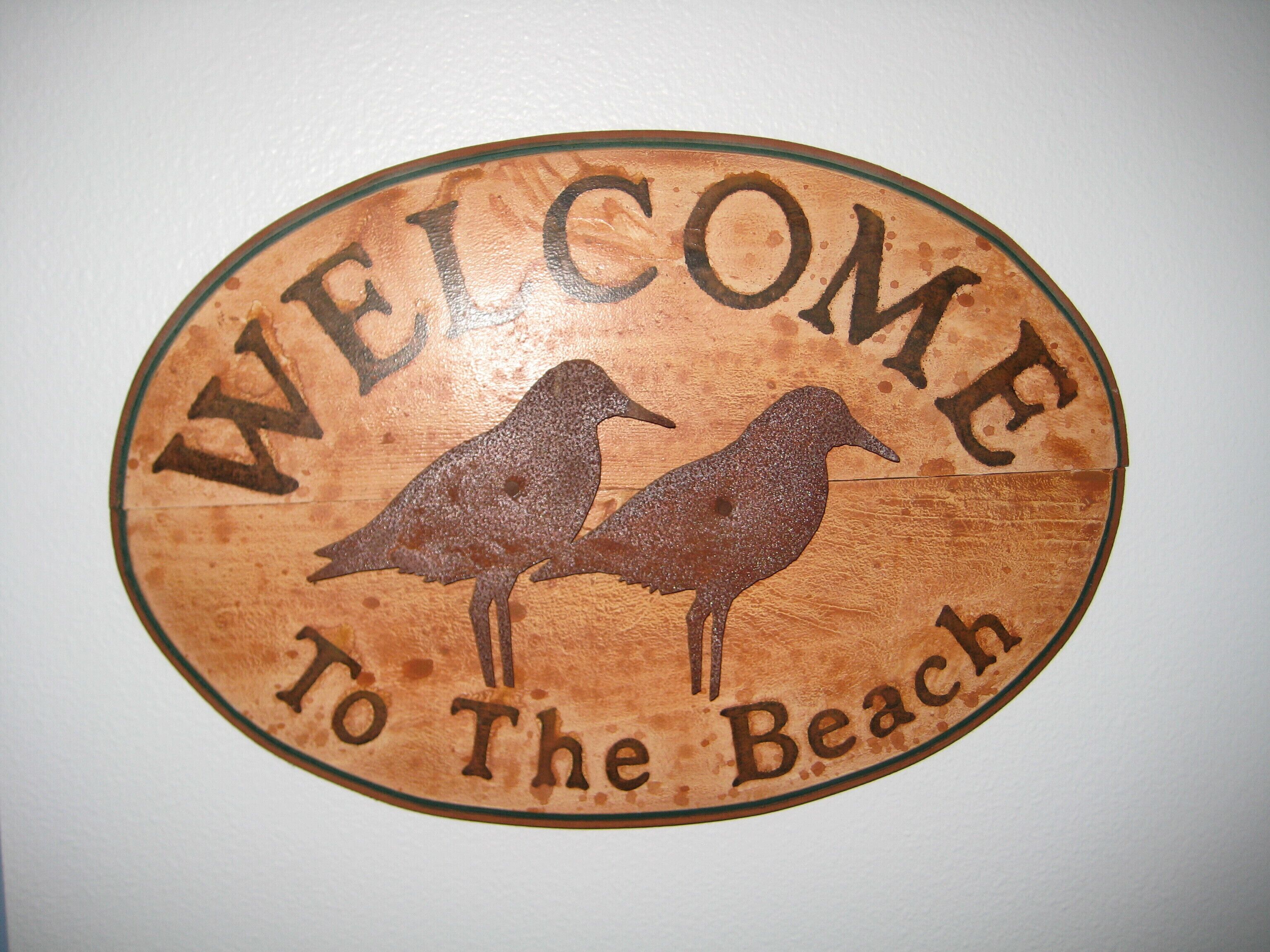 A wooden sign with two birds and the text "WELCOME To The Beach".