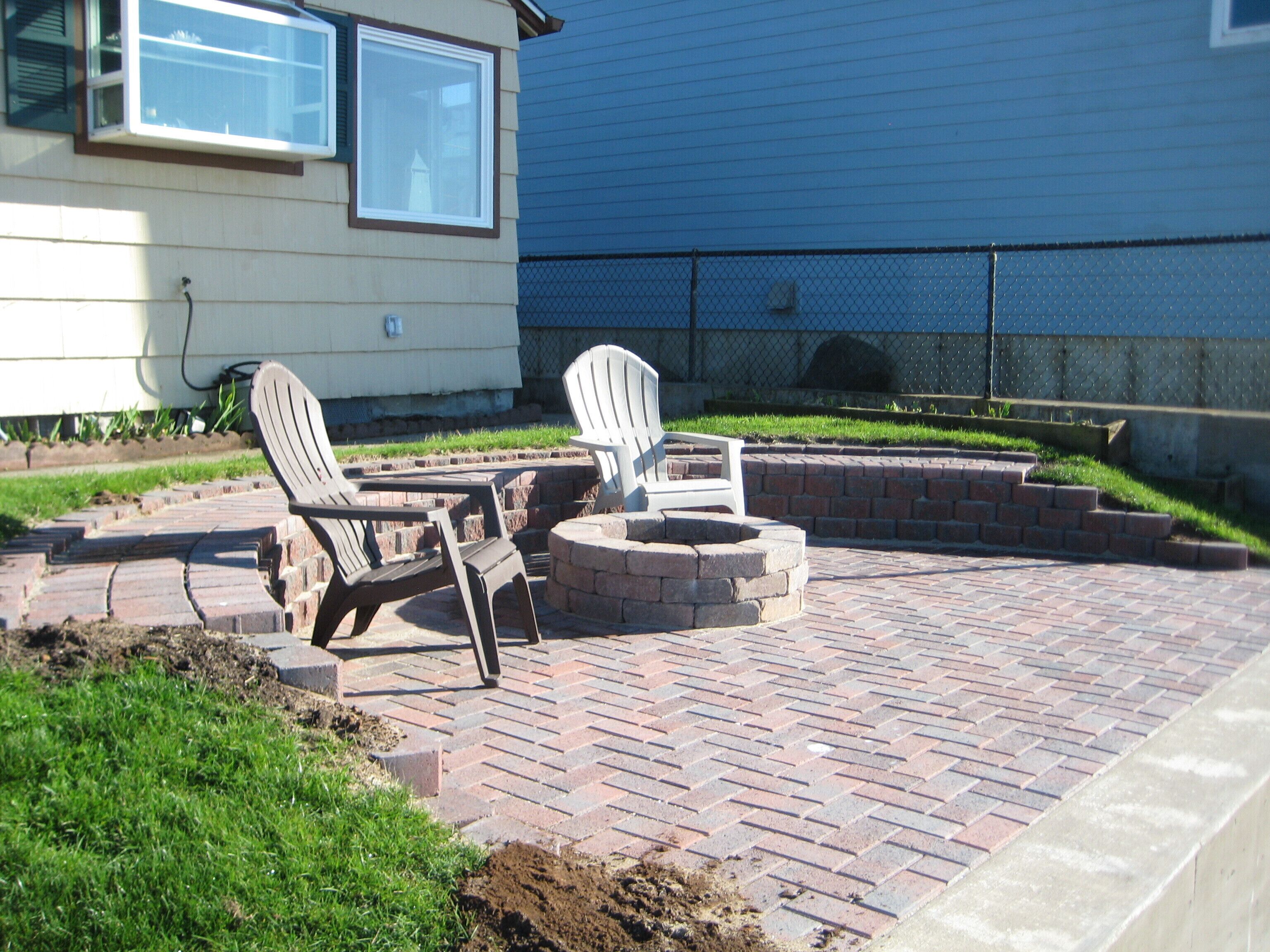 Un espace patio aménagé avec deux fauteuils Adirondack et un foyer en briques.