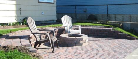 Un espace patio aménagé avec deux fauteuils Adirondack et un foyer en briques.