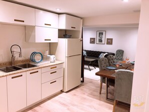 A compact kitchen with white cabinets, a built-in oven, and a sink. There is a dining area with a table and chairs, and a sofa in the background. - Two Bedroom Spacious Basement Unit (Toronto)