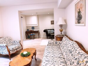 Ein Wohnzimmer mit einer Couch, zwei Sesseln, einem Couchtisch, einem Schreibtisch und einer Lampe.