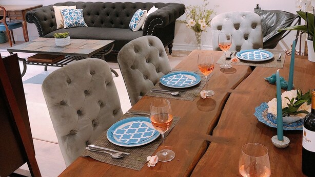 Un comedor con una mesa de madera dispuesta para dos personas, con platos azules estampados y copas de vino.