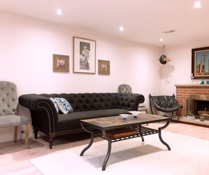 A living room with a black sofa, a wooden coffee table, a grey armchair, and a fireplace with a painting above it.