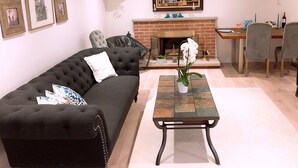 Una sala de estar con un sofá negro, una mesa de centro, una chimenea y un comedor con mesa y sillas.