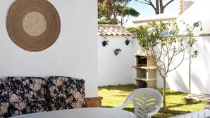 A patio with a round woven mat, a white chair, a sofa with floral cushions, and a small tree. - Chalet 'Poniente' with Pool and Garden (Roche)