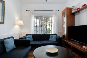 A living room with a sofa, a coffee table, a TV, and a window with curtains. - Chalet 'Poniente' with Pool and Garden (Roche)