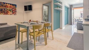 A modern living room with a dining area, a TV mounted on the wall, and a colorful painting. - Palermo by Interhome (Balestrate)