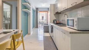 A modern kitchen with white cabinets, a microwave, and a dining area with a yellow chair. - Palermo by Interhome (Balestrate)