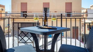 A balcony with a table set for two, featuring a bottle and glasses of white wine, overlooking a building with red shutters. - Palermo by Interhome (Balestrate)