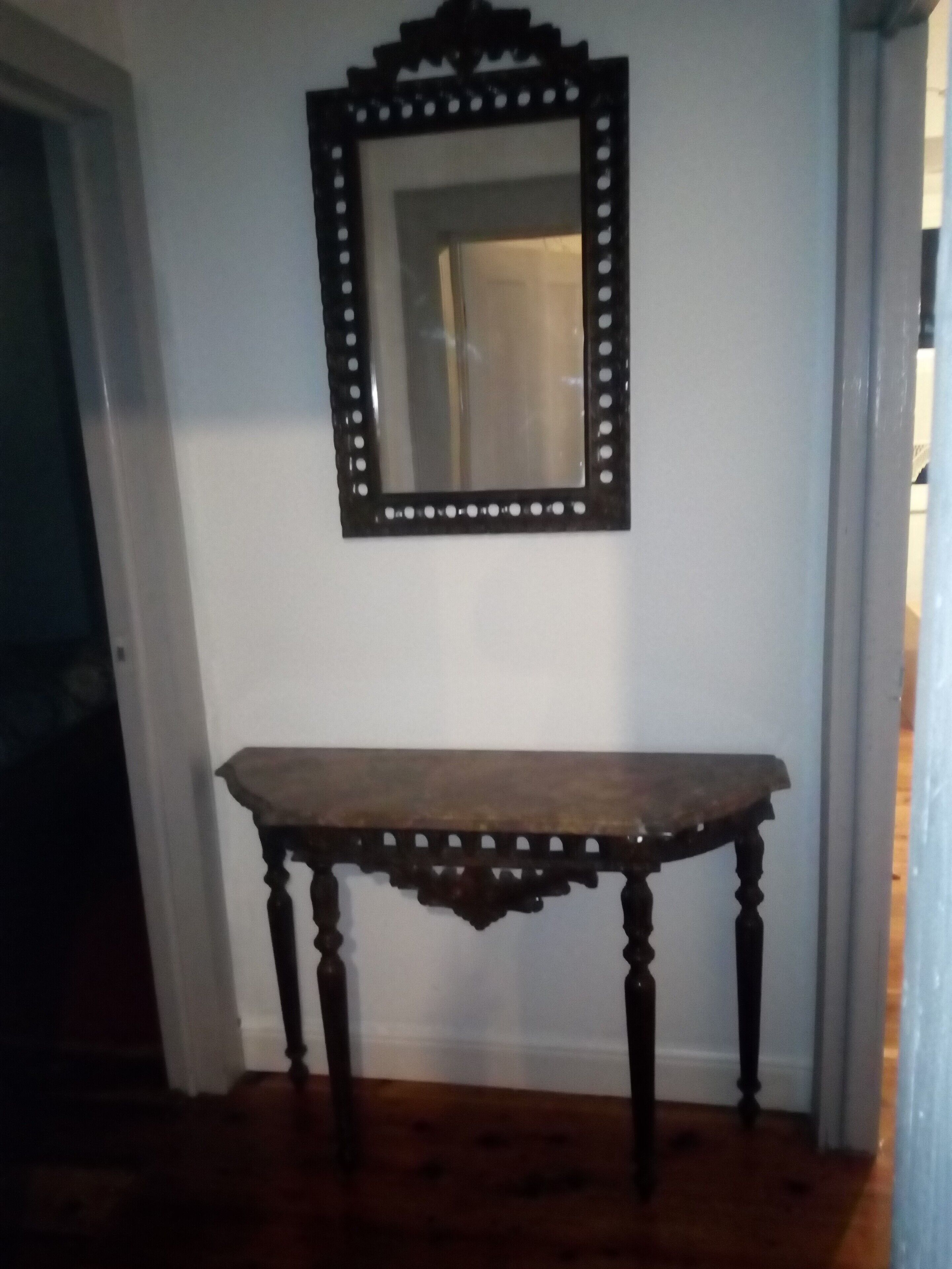 Una mesa de madera oscura con patas ornamentadas y un espejo con marco decorativo.