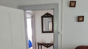 A room with a wooden floor, a white door, a mirror on the wall, and a chair.