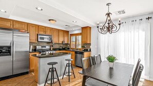 A modern kitchen with wooden cabinets, stainless steel appliances, and a central island with stools. - Luxe 3 Bedroom Home with optional Heated Pool 🌊 6Mi to LV Strip!💫✨ (Las Vegas)